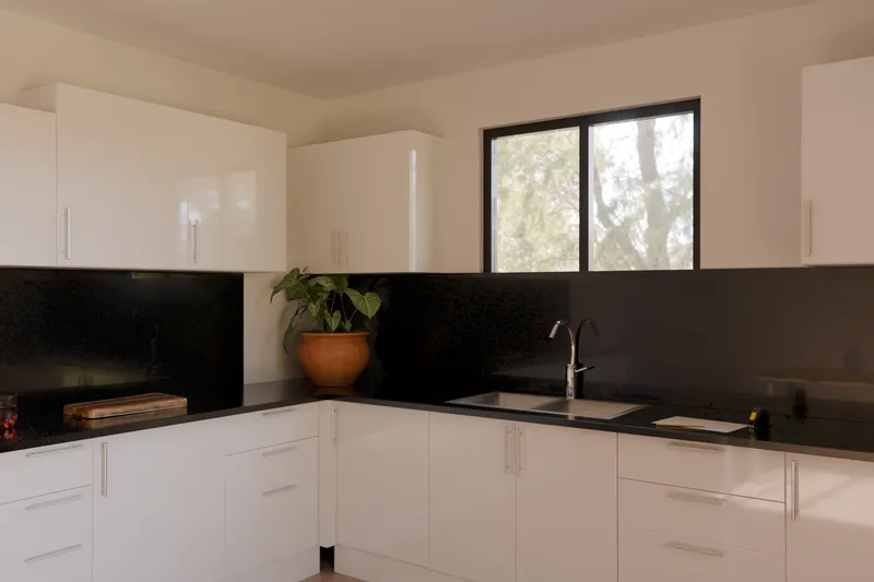 An L-shaped gloss white kitchen with a black granite benchtop and a window over the sink