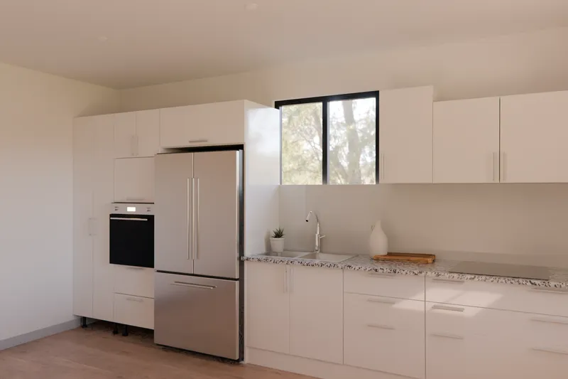A one-wall gloss white kitchen with a pantry, oven tower and fridge beside a dining table